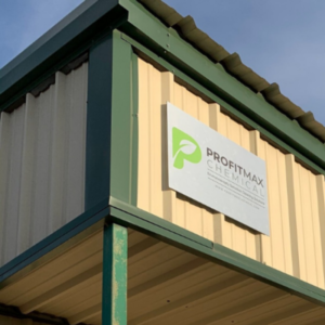 Una imagen de la esquina del edificio químico ProfitMax. Una blusa color canela con bordes verdes y un cartel plateado con el logo de ProfitMax Chemical y palabras en él.