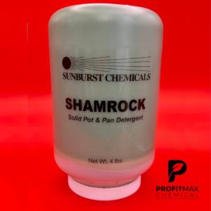 An image graphic of the Shamrock chemical that is contained in a green jar with a white lid. The jar presents black text atop a clear label. The label presents the text in a vertical alignment. The black text attached to the label has the word Sunburst placed on top of the jar with their logo sitting right above that. The Sunburst logo is a black circle representing a sun with black lines representing rays that shoot to the right which covers the word, Sunburst. Below that is the chemical name, Shamrock, that sits right above the description. The description is a Solid Pot & Pan Detergent. Below, is the Net Wt close to the white cap. The text Net Wt in black text is followed by 4 lbs. To the right of the jar at the bottom of the image is the ProfitMax P logo in white text. To the right, in black text is ProfitMax atop of the word Chemical in black text. The image graphic is placed in front of a cherry red backdrop.