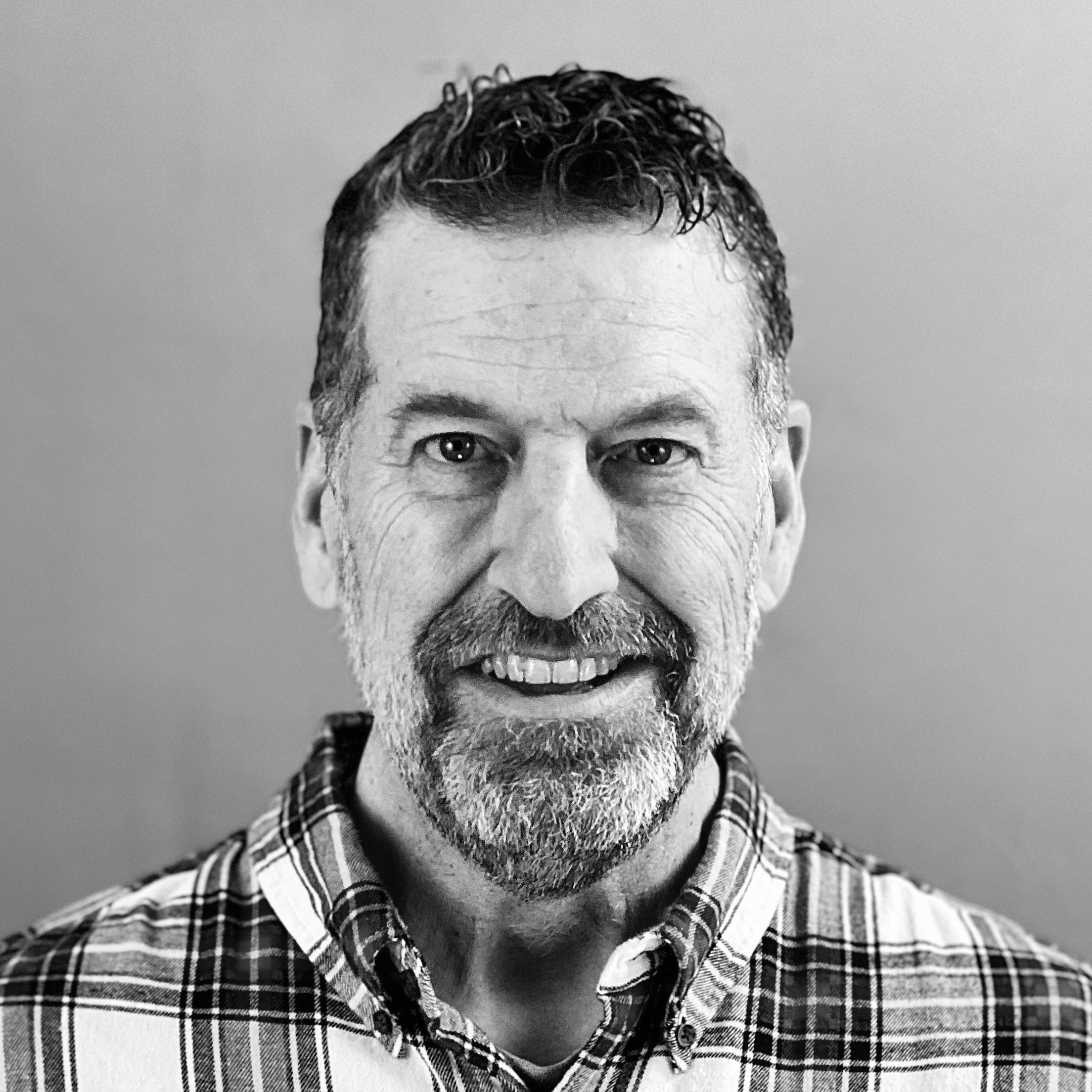 Una imagen de Brian Bluhm sonriendo con una camisa a cuadros en un retrato en blanco y negro